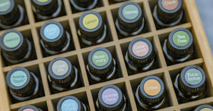 A wooden storage box filled with 100% natural essential oil vials, each labeled with a colorful cap sticker.