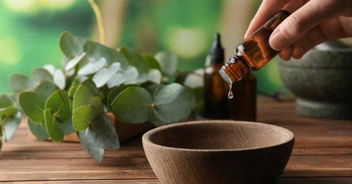 A woman pouring out essential oil from a glass vile into a wooden diffusion bowl. She prepares to practice aromatherapy.