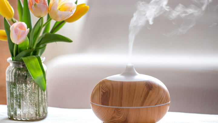 A white and brown essential oil diffuser on a coffee table dispenses a cloud of aromatic scents into the living room.